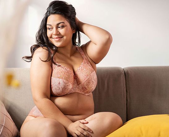 Kurviges Model sitzt auf einem Sofa und trägt Dessous in großen Größen.