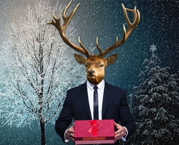 Mann im Anzug mit Hirschkopf hält ein Körpernah-Geschenk in den Händen.